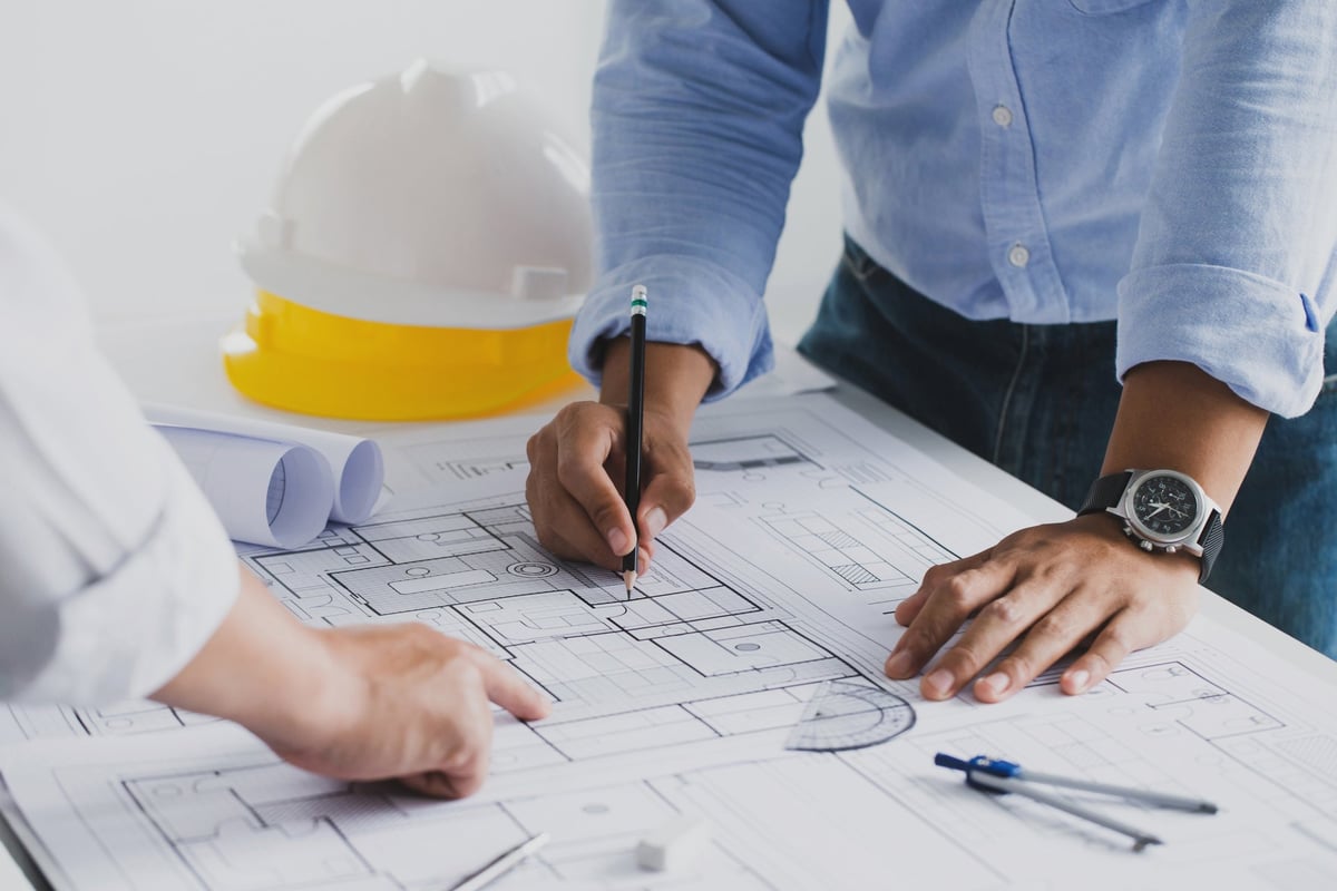 Engineers collaborating over an architectural blueprint at a workstation